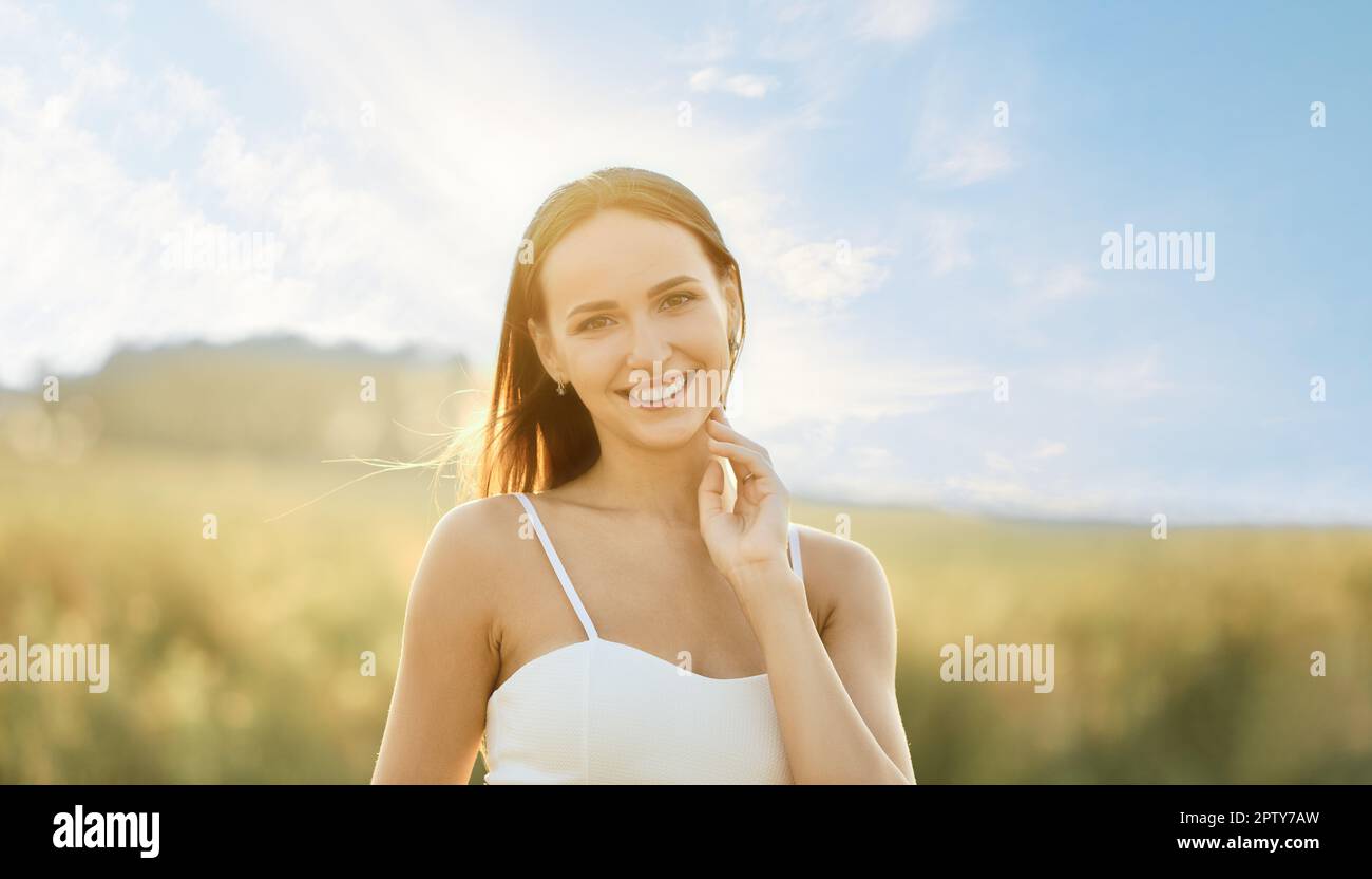 Porträt einer lächelnden jungen Frau im Spaghetti-Gurtkleid auf dem Feld mit der Sonne im Hintergrund Stockfoto