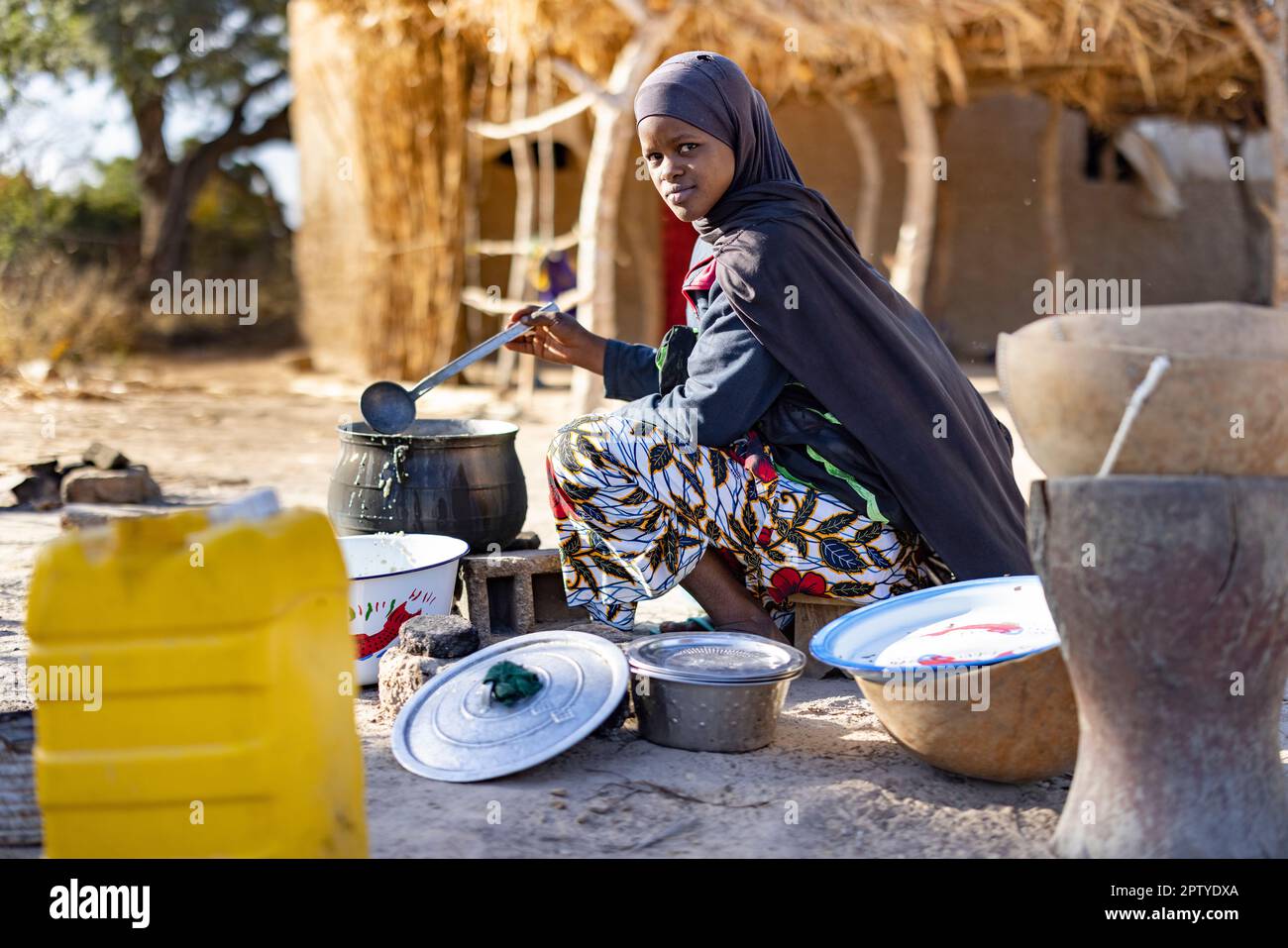 Eine junge Fulani-Flüchtlingsfrau, die aus dem Konflikt im Norden vertrieben wurde, kocht bei einem offenen Feuer in der Region Segou, Mali, Westafrika, Essen. 2022 Dürre und Hungerkrise in Mali. Stockfoto