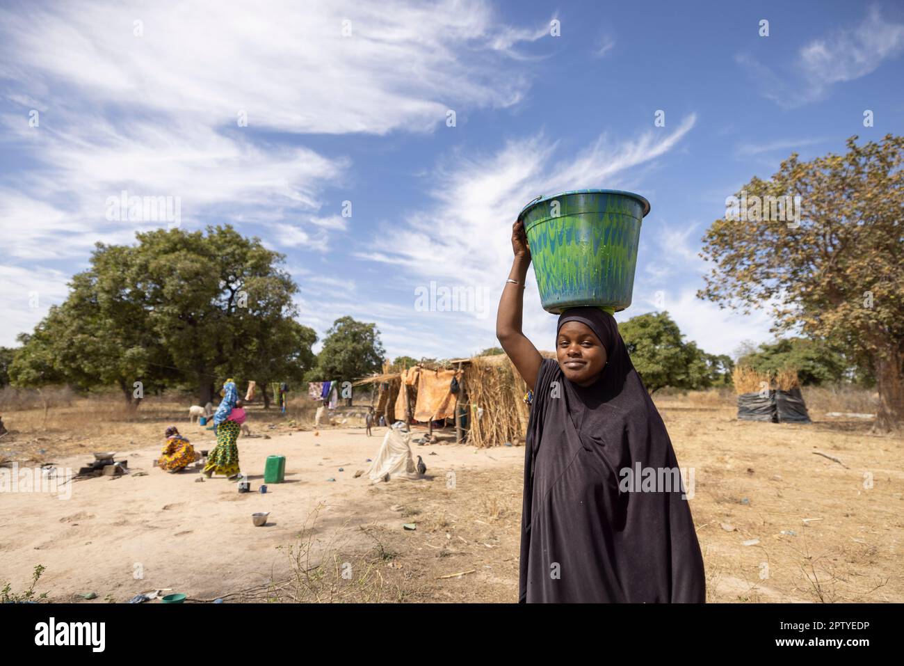 Eine junge Frau trägt einen Eimer Wasser, der auf ihrem Kopf ausbalanciert ist, aus dem Brunnen in der Region Segou, Mali, Westafrika. 2022 Dürre und Hungerkrise in Mali. Stockfoto