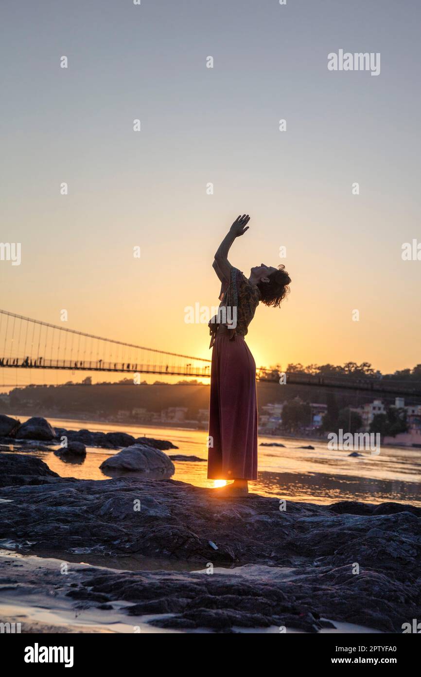 Indien, Uttarakhand, Rishikesh, Ganga, Ganges-Ufer. Eine Frau, die Yoga praktiziert. Sonnenuntergang. Stockfoto
