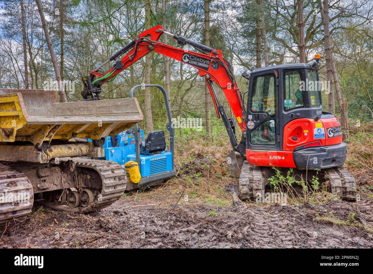 Ein Kipperwagen und Bagger von Cheshire UK vom April 2023 reparieren einen Weg in Delamere Forrest, während sie einen Löffel mit Erde füllen, Teil der Baumaschinen Stockfoto