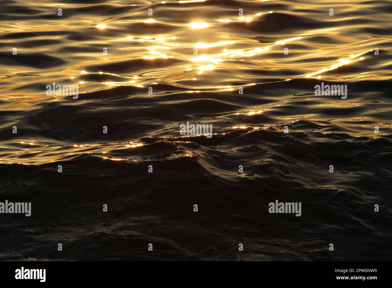 Goldener Sonnenuntergang auf dem Meer leuchtend farbenfrohes Orange, gelbe Linie der letzten Sonnenstrahlen, Sonnenschein auf ruhigem, dunklem Wasser mit wenig Brise, Wassertextur. Stockfoto