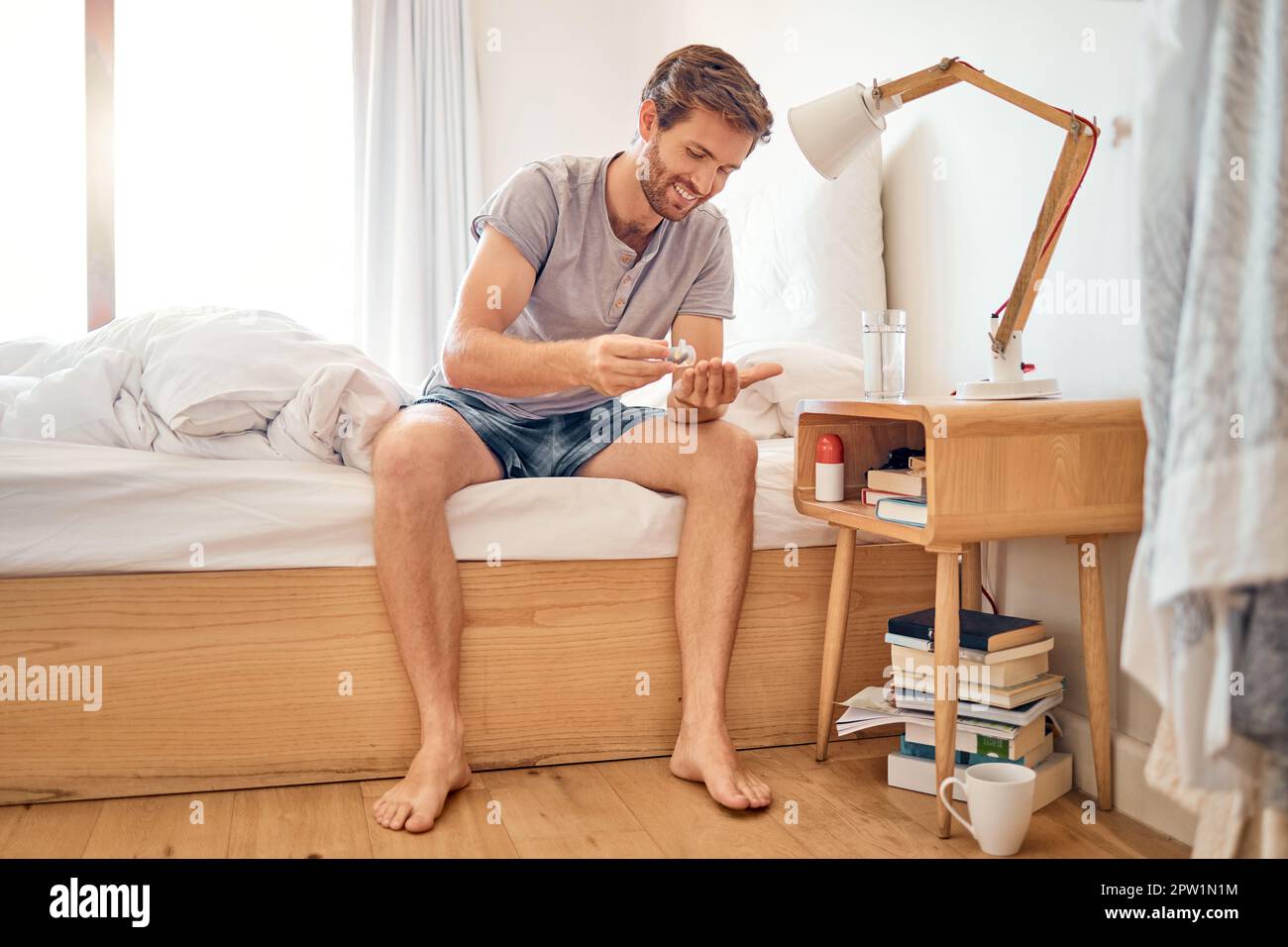 Bett, Pillen und Medizin eines glücklichen Mannes, der seine Morgenmedikamente zu Hause im Schlafzimmer nimmt. Männlich in Selbstmedikation, Antibiotika und Rezept Stockfoto