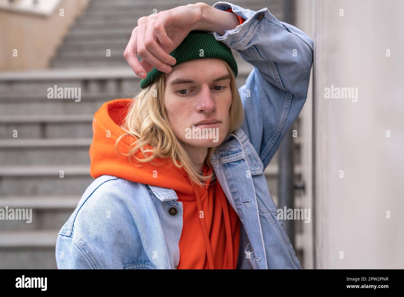 Ein aufgebrachter Millennials-Typ, der sich an eine Betonwand lehnte, während er auf einer Fußgängertreppe stand Stockfoto