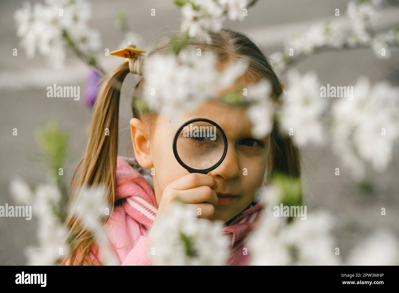 Kind lernt etwas über die Umwelt. Naturerziehungsaktivität für den Welt-Erde-Tag. Im Frühling auf Erkundungstour, blühende Blumen im Garten. Ein ernstes Mädchen Stockfoto