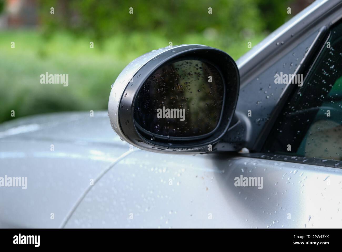 Nahaufnahme des Außenspiegels am Fahrzeug nach Autowaschanlage oder Regen mit isoliertem grünem Hintergrund. Autospiegel, um hinter das Auto zu sehen. Stockfoto