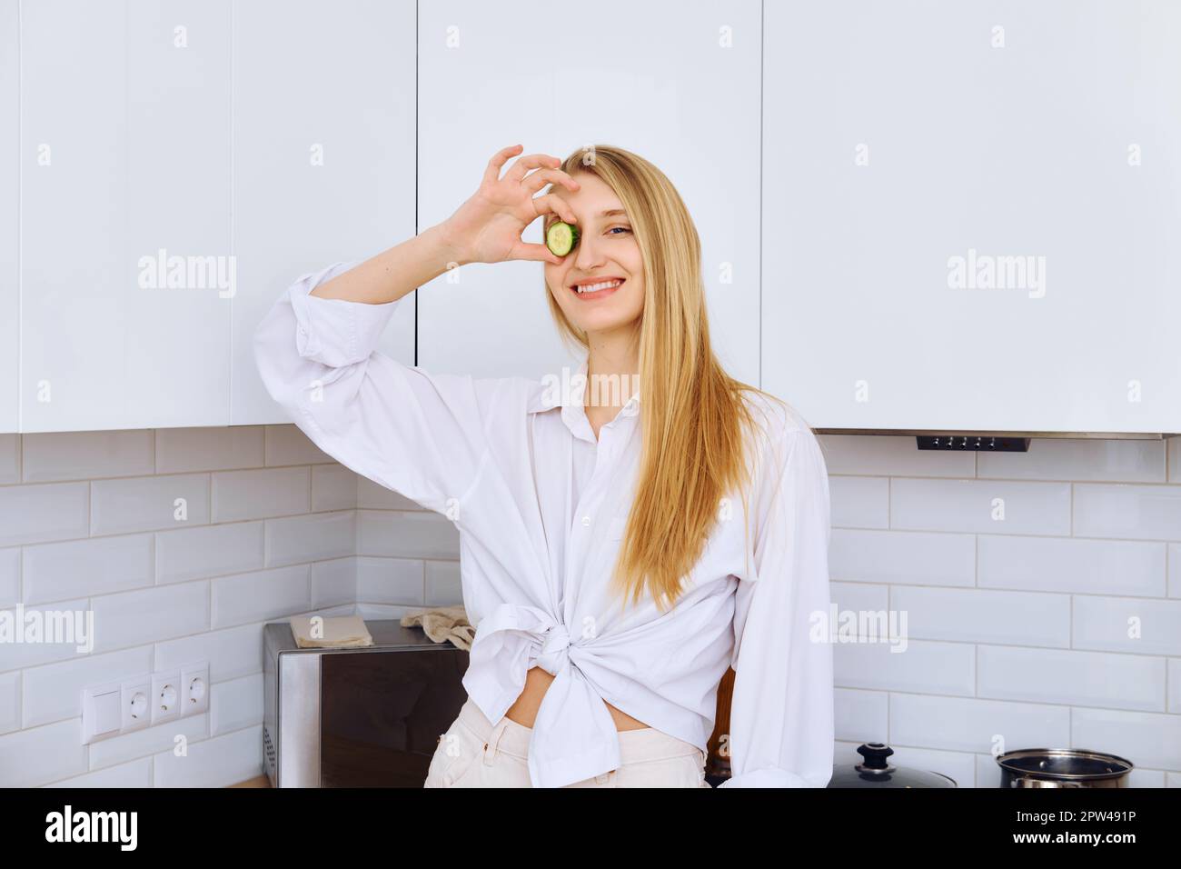 Kindische junge Frau gab beim Kochen eine Gurkenscheibe auf ein Auge Stockfoto