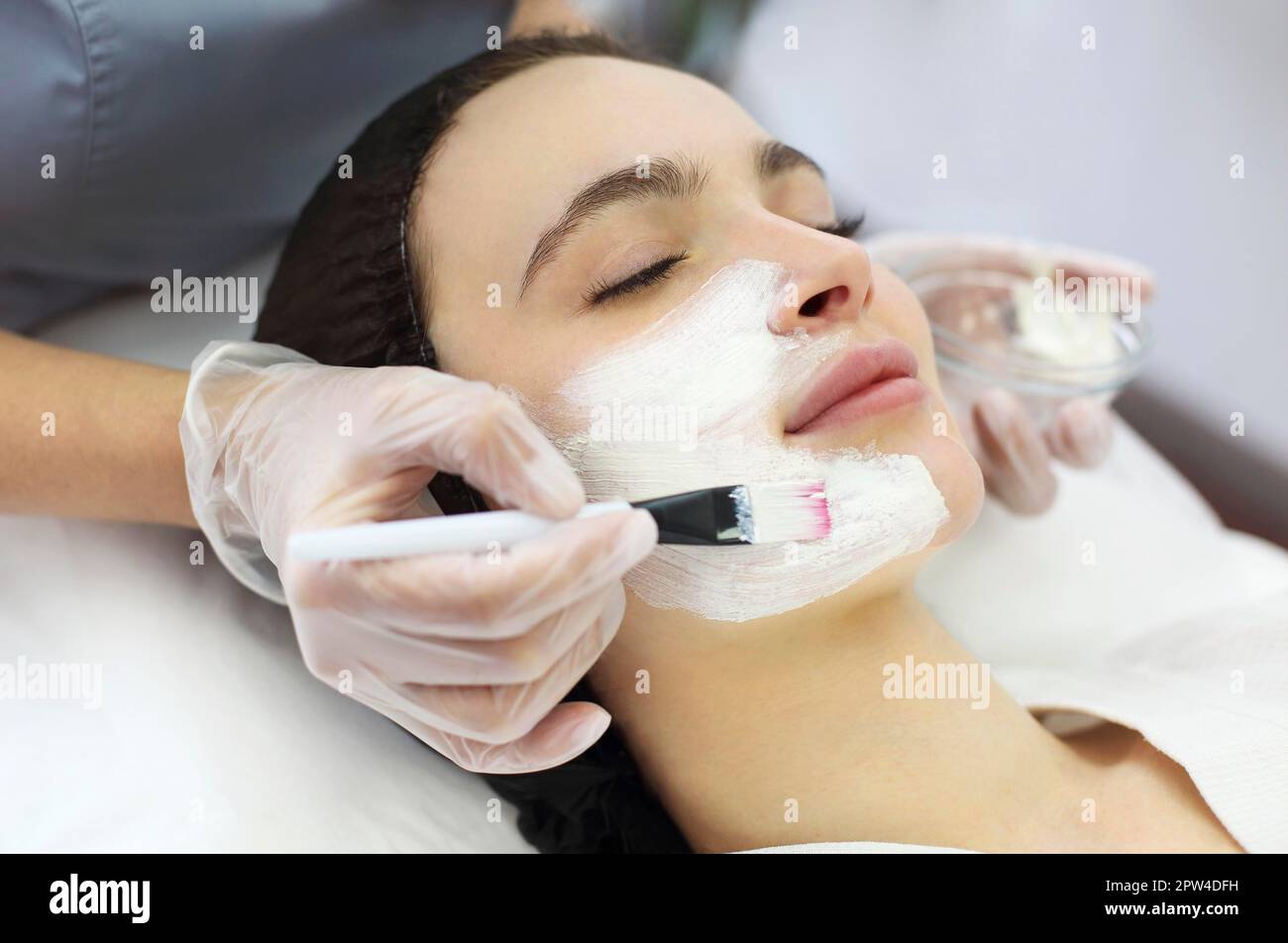 Unkenntlich weibliche Kosmetikerin Anwendung Tonmaske mit Pinsel auf Gesicht Der entspannten Client während der Hautpflege Verfahren im Spa-Salon Stockfoto