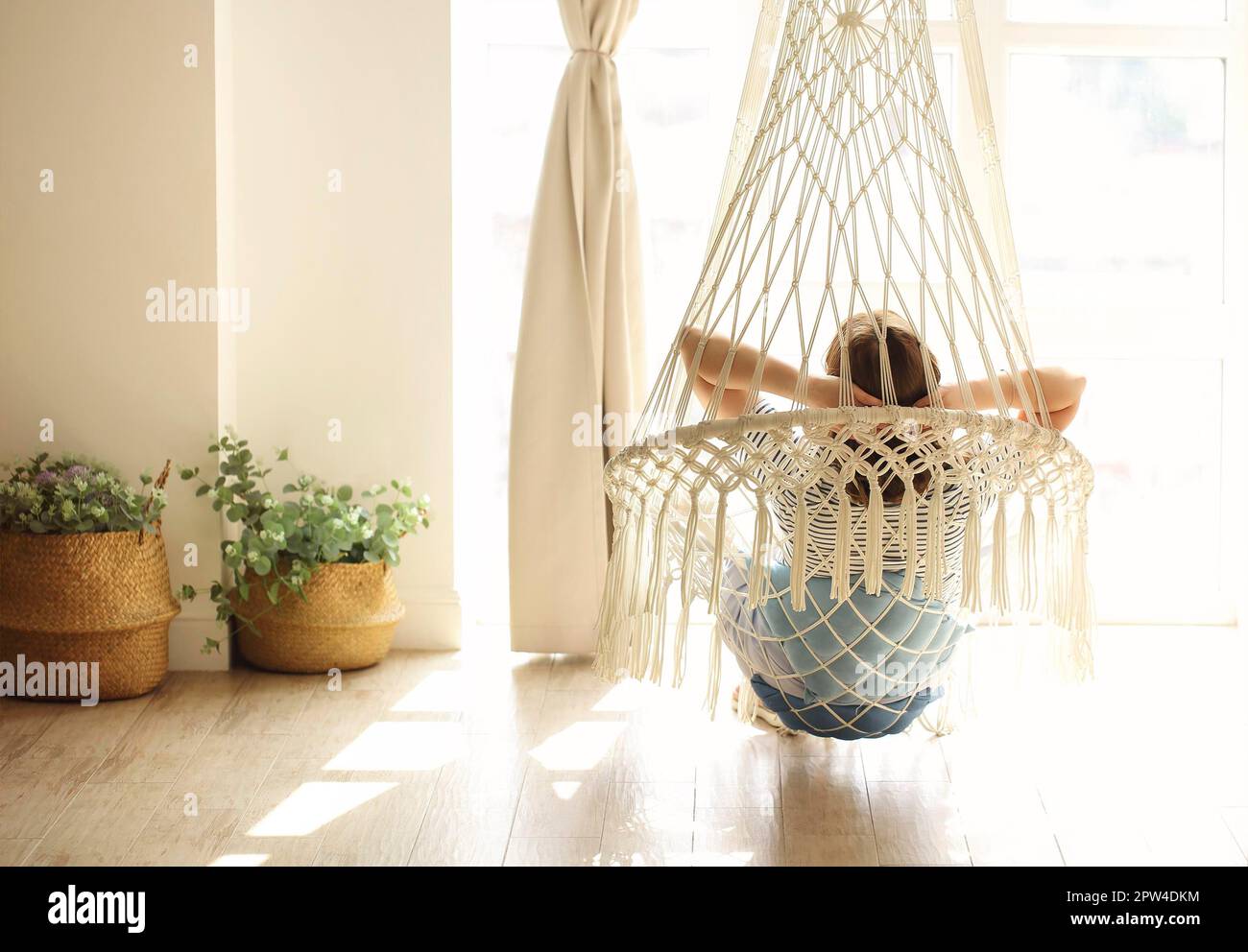 Verträumte Frau, die im Hängesessel liegt und das Wochenende genießt Gemütliches Zimmer mit Sonnenlicht Stockfoto