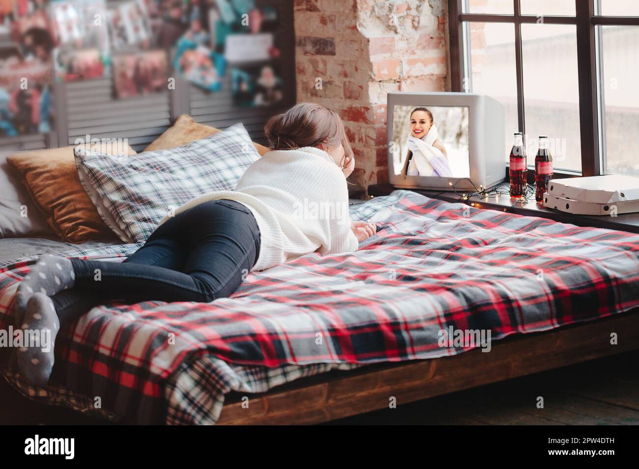 Unkenntliche Frau, die sich auf einem bequemen Bett mit karierter Decke entspannt und zu Hause Retro-TV guckend Stockfoto