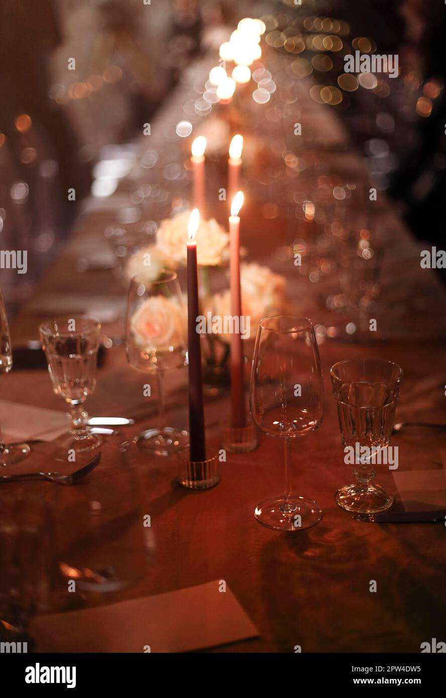 Brennende Kerzen und frische Blumen auf dem Banketttisch neben Tellern und Glaskelchen am Abend Stockfoto