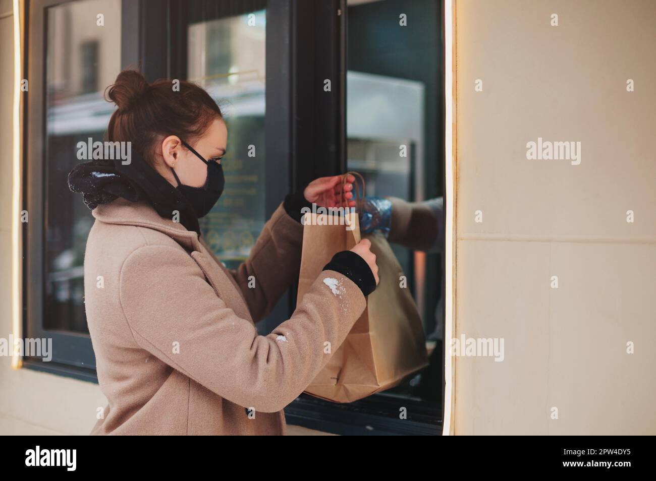 Seitenansicht einer Kundin, die während einer Pandemie einen Papierbeutel mit Essen zum Mitnehmen aus dem Restaurantfenster nimmt Stockfoto