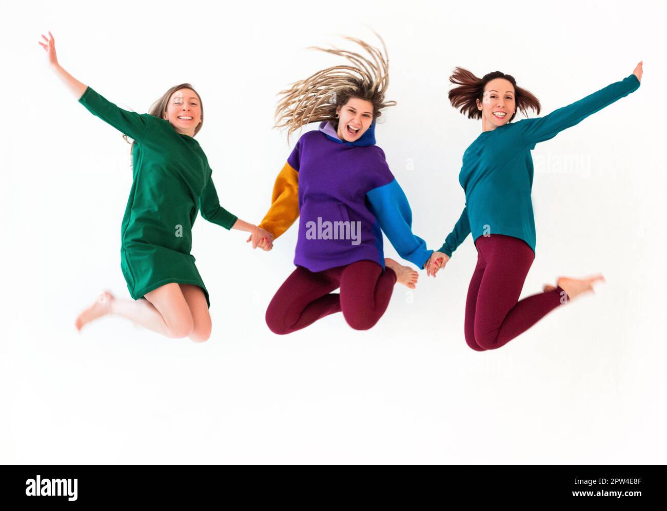 Bild von drei fröhlichen, verspielten Barfußfrauen unterschiedlichen Alters, die sich an den Händen halten, springen und Spaß haben, Urlaub genießen, feiern Stockfoto