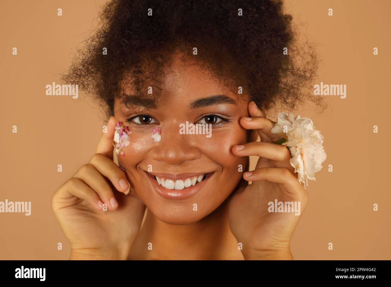 Porträt eines wunderschönen dunkelhäutigen Models mit hohem Afro-Haarschnitt und natürlichem Make-up mit Blütenblättern auf einer Seite ihres Gesichts enthält die pinkfarbene Nelkenblume Stockfoto