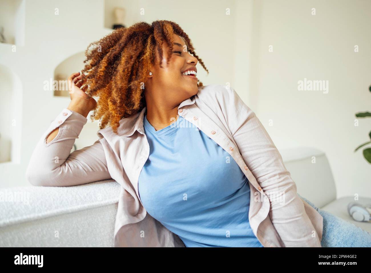 afroamerikanische Millennial-Mädchen, zufrieden und glücklich, sitzen auf einem bequemen Sofa in gemütlichen modernen hellen Wohnzimmer. Genießen Sie ihr Leben Stockfoto