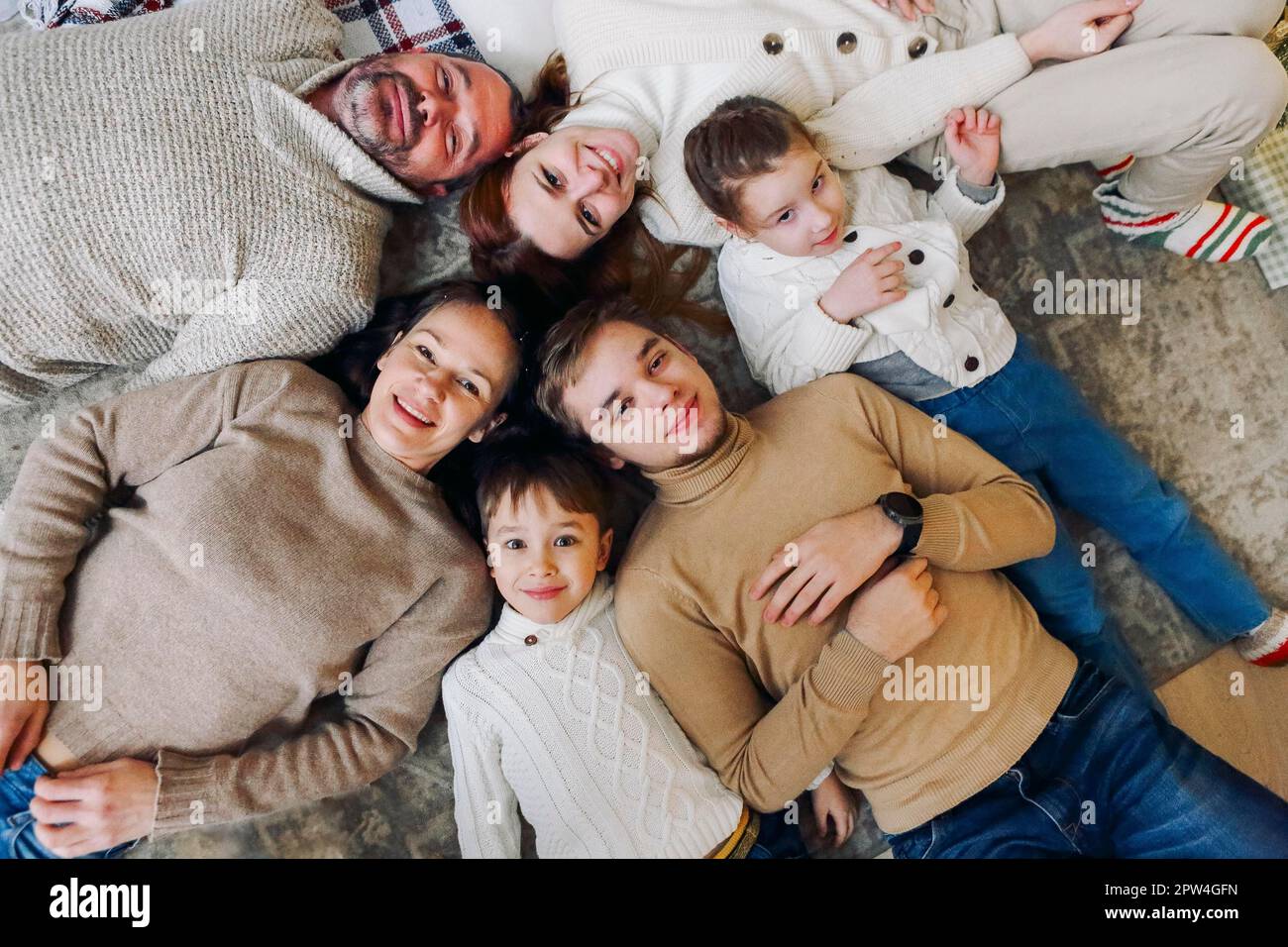 Draufsicht auf eine glückliche, große, mehrgenerationale Familie, die im Kreis auf dem Boden liegt und vor der Kamera lächelt, Bindungen stärkt und gesunde Beziehungen aufbaut Stockfoto