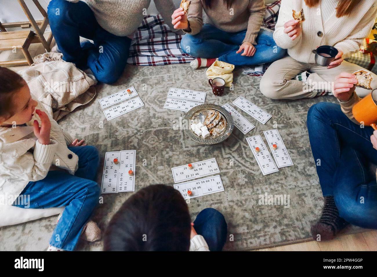 Große Familie mit Kindern, die auf dem Boden neben dem Weihnachtsbaum sitzen und gemeinsam Lotto-Brettspiele spielen, während sie an Weihnachten in gemütlichen Wohnungen verbringen Stockfoto