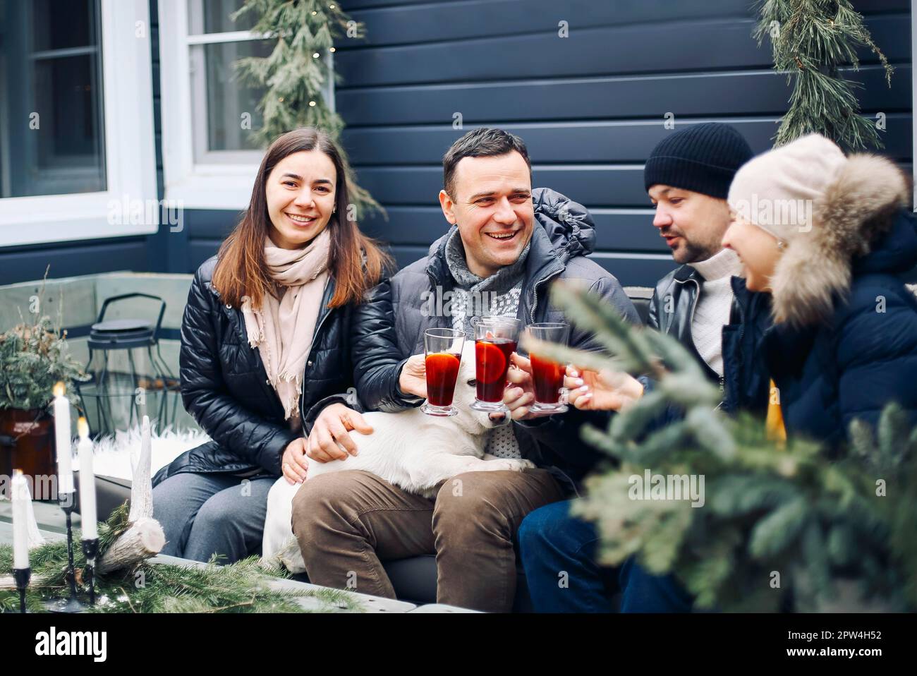 Lagerfeuer-Party. Fröhliches junges Familienpaar, das sich im Winter mit Freunden am Lagerfeuer versammelt, glückliche Menschen, die heißen Glühwein zubereiten und trinken Stockfoto