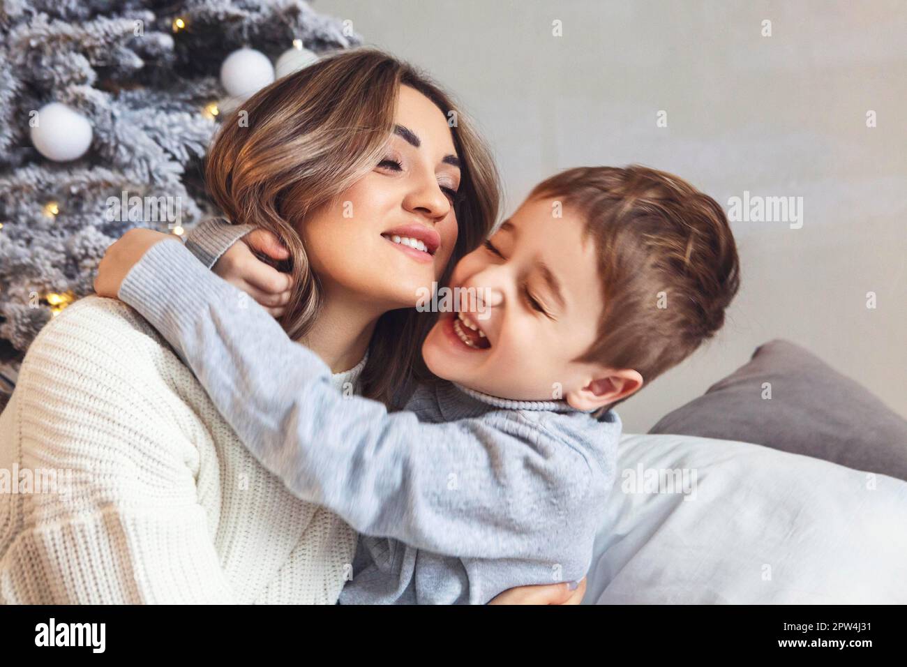 Ein kleiner Vorschuljunge hilft Mutter beim Dekorieren des Weihnachtsbaums zu Hause, mutter und kleiner Sohn schmücken zusammen Weihnachtsbaum, junge Familieneltern und Stockfoto