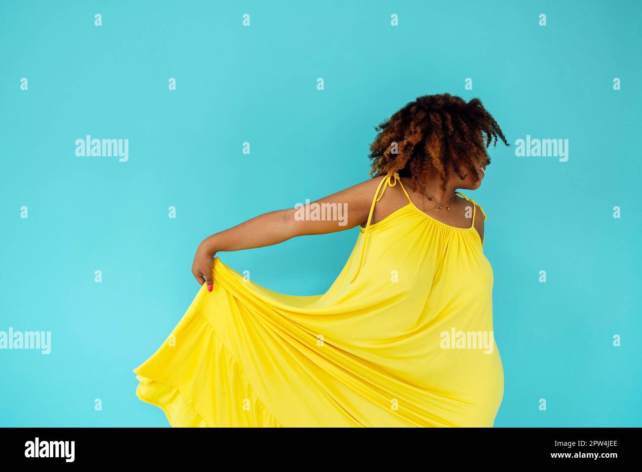 Schöne helle fröhliche afrikanische Frau in gelbem Kleid im blauen Studio-Hintergrund Stockfoto