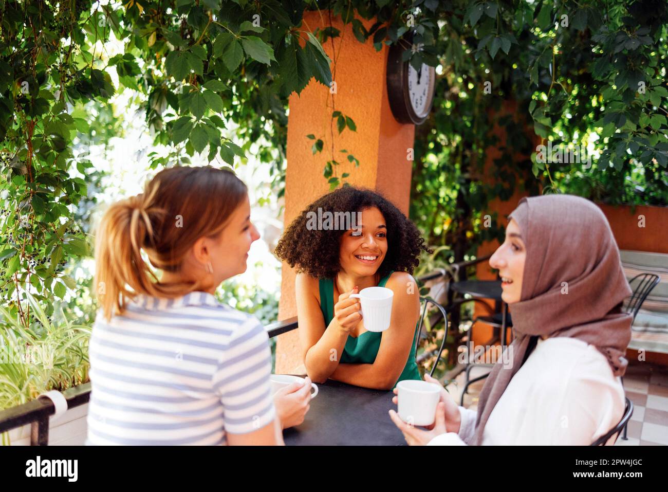Multiethnische Gruppe von Mädchen, die lässige Kleidung und traditionelle Hidschab-Bindung tragen und Spaß im Freien haben. Drei junge Mädchen im Gartencafé Stockfoto