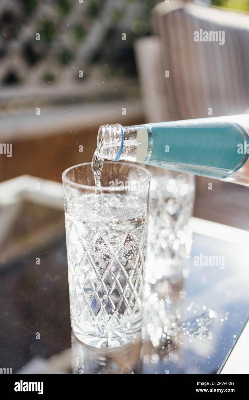 Sprudelndes Wasser aus der Flasche in das Glas gießen. Wassergetränk, das in Glas fließt, Gartenhintergrund. Nahaufnahme Stockfoto