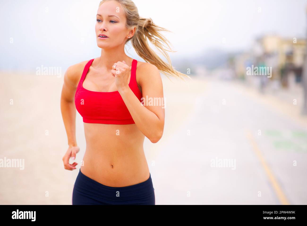 Sie treibt sich bei jedem Lauf weiter. Eine junge Frau, die am Strand joggt Stockfoto