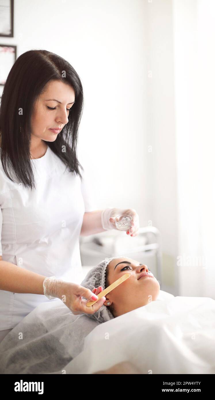 Nicht erkennbarer Kulturkosmetologe, der Gel auf das Gesicht einer jungen Frau im Schönheitssalon anwendet Stockfoto