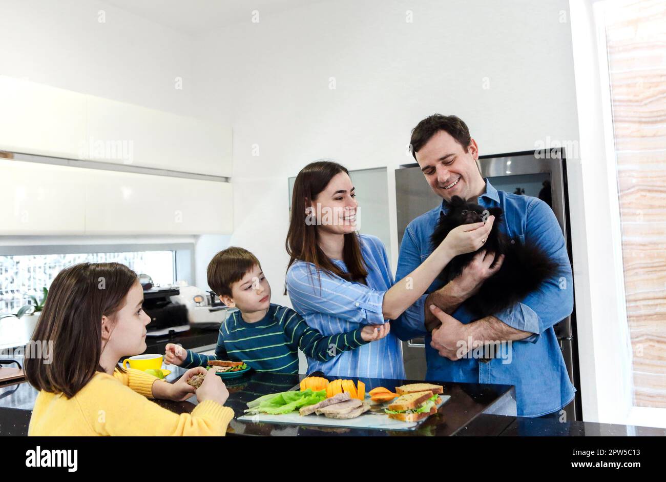 Glückliche fröhliche Familie genießen gesundes Frühstück zusammen in der Küche zu Hause Wochenende mit kleinen lustigen Hund Stockfoto