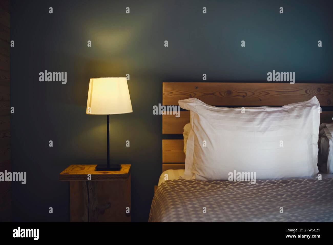 Nachtszene im gemütlichen Zimmer, Nachttisch mit Lampe. Schlafzimmerlampe auf dem Nachttisch neben dem Schlafbett Stockfoto