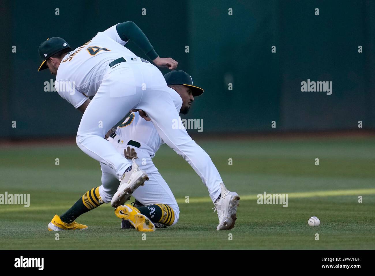 Oakland Athletics left fielder Tony Kemp, bottom, tries to field a base hit by Cincinnati Reds' Henry Ramos under shortstop Kevin Smith during the second inning of a baseball game in Oakland, Calif., Friday, April 28, 2023. (AP Photo/Jeff Chiu) Stockfoto
