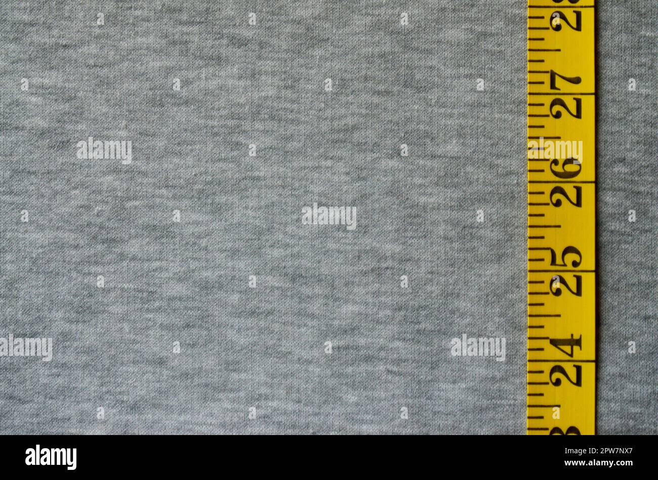 Gelbe Maßband mit numerischen Indikatoren in Form von Zentimeter oder Zoll liegt auf einem grauen Gestrick. Konzept der Industrie in Verbindung mit s. Stockfoto