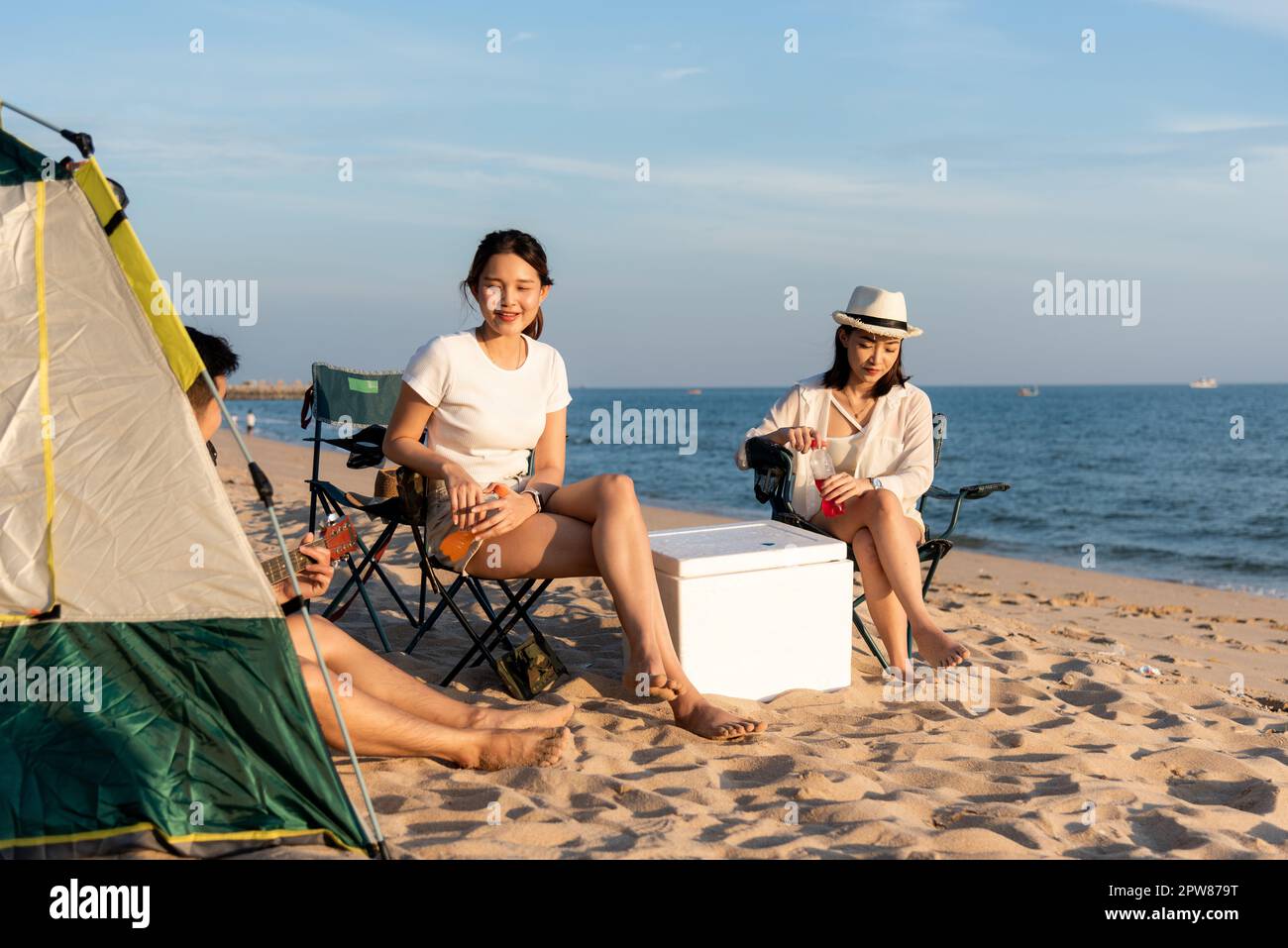 Glückliche Freunde mit Getränken im Camp und lachen zusammen in Urlaub am Sandstrand in der Nähe Camping Zelt Urlaubszeit bei Sonnenuntergang, Junge asiatische Gruppe Frau A Stockfoto