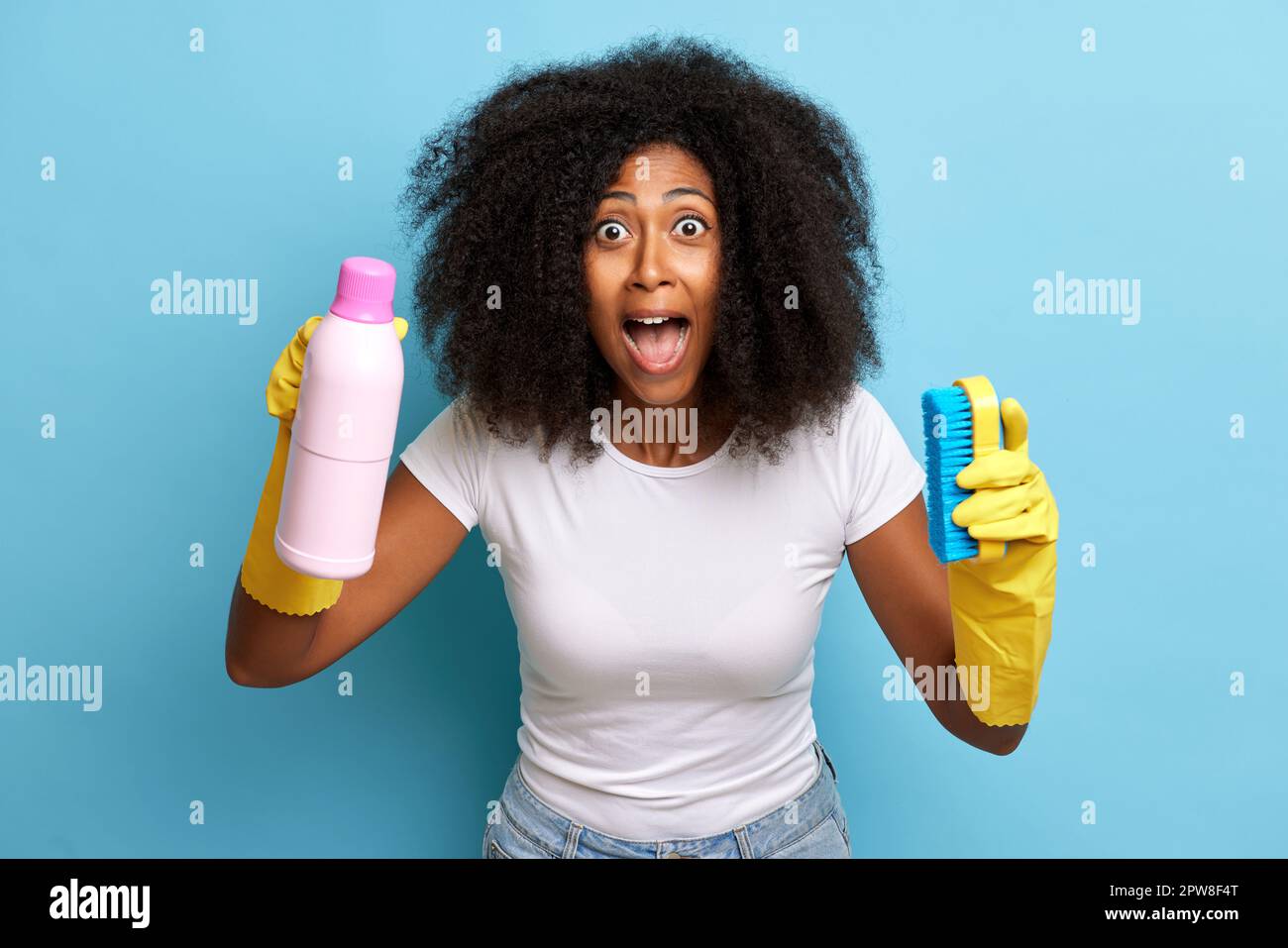 Eine überraschte afroamerikanische junge Frau hat Reinigungsmittel und trägt Schutzhandschuhe aus Gummi, gekleidet mit legerem Stoff. Hochwertiges Foto Stockfoto