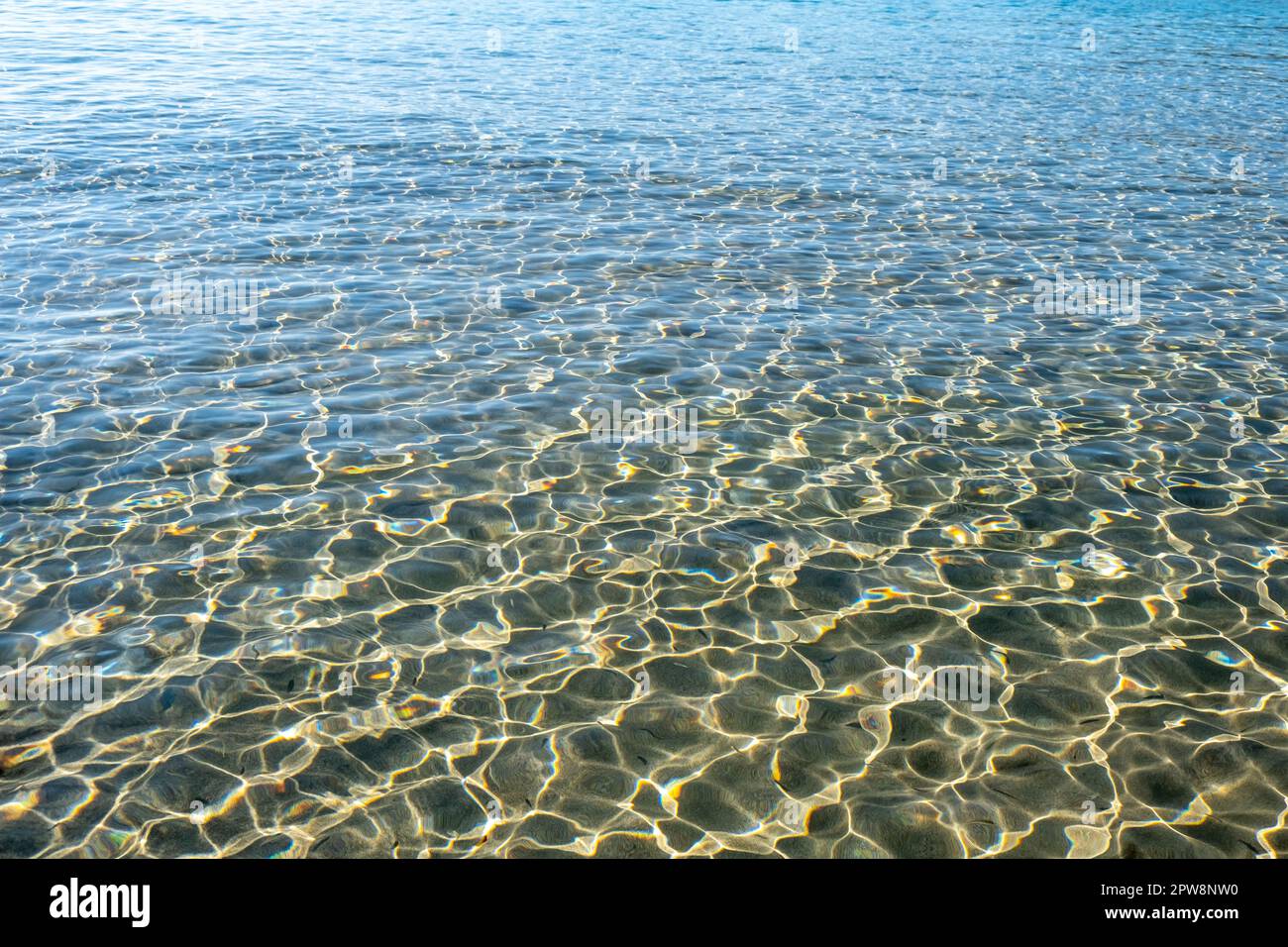 Transparenter ruhiger blauer Meerwasserhintergrund, Textur. Sonnenlicht reflektiert auf dem Ozean und lässt die Oberfläche und den sandigen Meeresboden glitzern. Leerzeichen Stockfoto