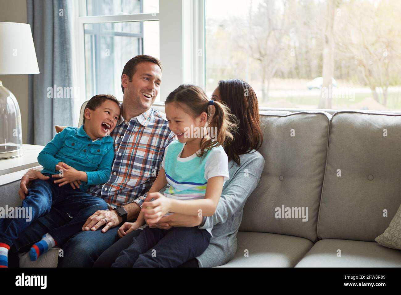 Keine Zeit ist wichtiger als die Zeit mit der Familie. Eine glückliche, junge vierköpfige Familie, die sich zu Hause auf dem Sofa zusammenhält. Stockfoto