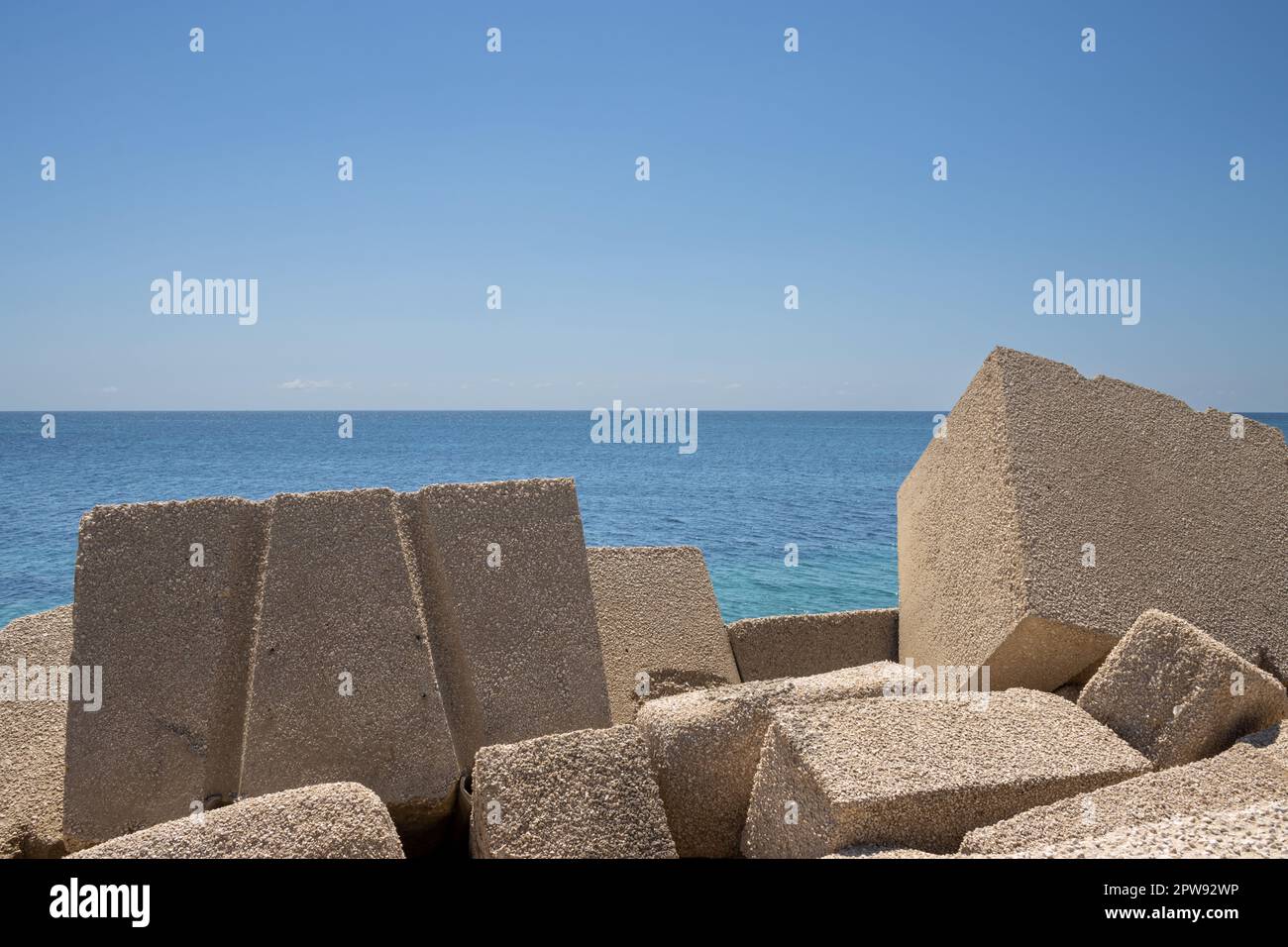 Riesige kubische Objekte aus Beton, die als Meereswand im lokalen Yachthafen verwendet wurden. Ruhiges Wasser des Mittelmeers (Tyrrhenisches Meer). Blauer Himmel in der frühen Sprotte Stockfoto