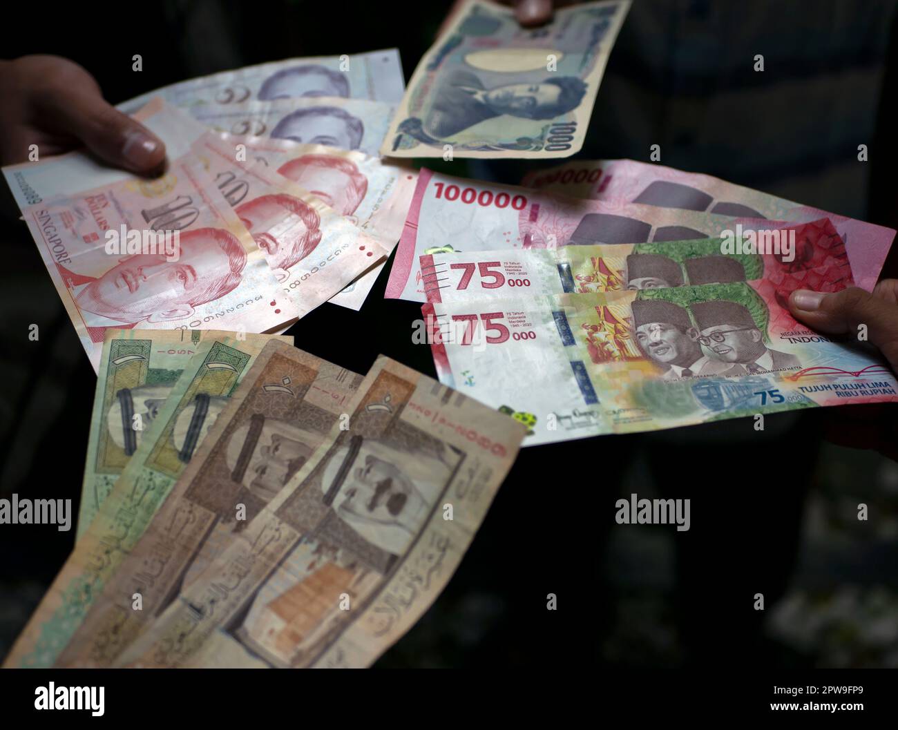 Asiatisches Kind mit indonesischem Rupien, Singapur-Dollar, Saudi-Arabien-Rial und Japan-Yen-Geld, ausgewählter Fokus Stockfoto