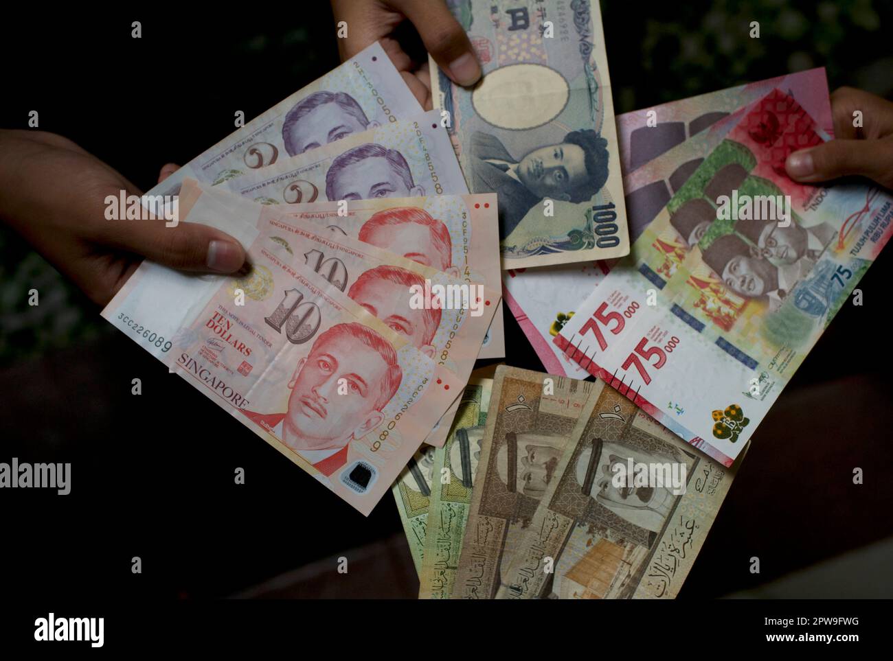 Asiatisches Kind, das indonesische Rupien, Singapur-Dollar, Saudi-Arabien-Rial und Japan-Yen-Geld hält, oberflächliche Konzentration Stockfoto