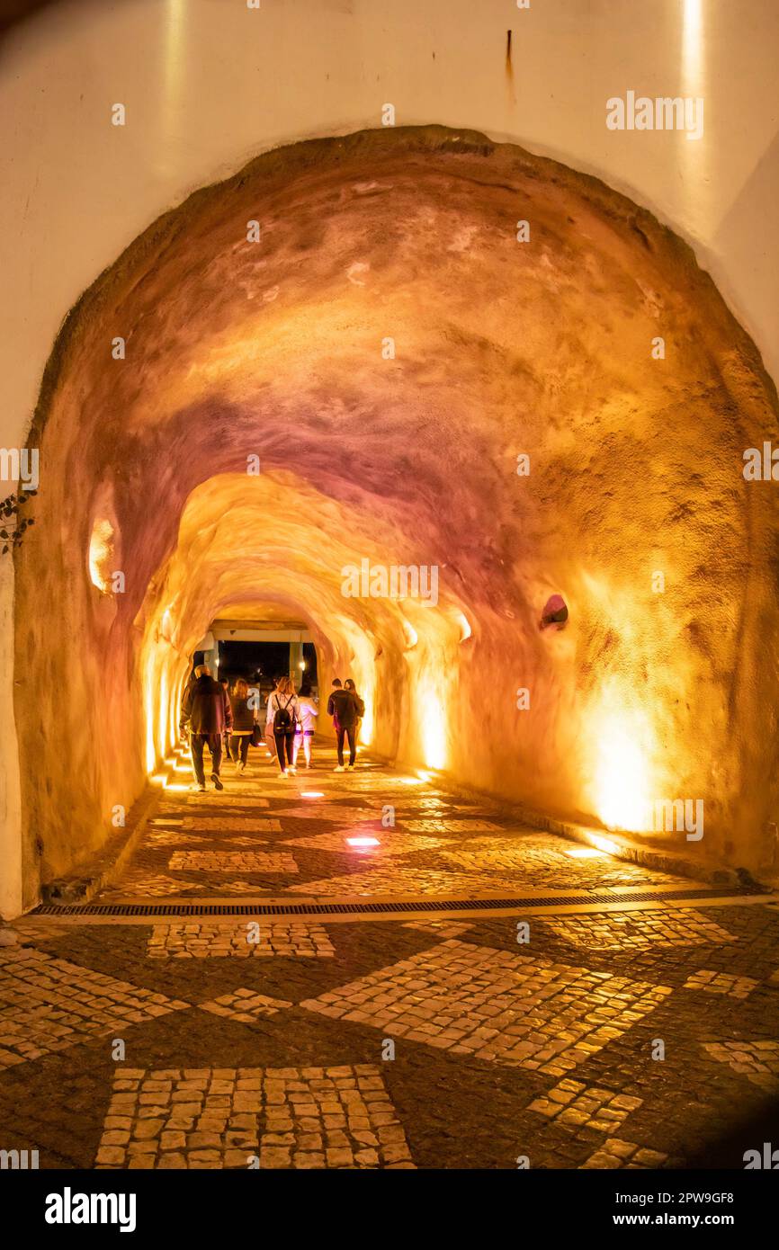 Ein wunderschön beleuchteter Tunnel mit einem kopfsteingepflasterten Pfad, in dem Menschen bei Nacht durch die beleuchtete Passage gehen. albufeira portugal Stockfoto