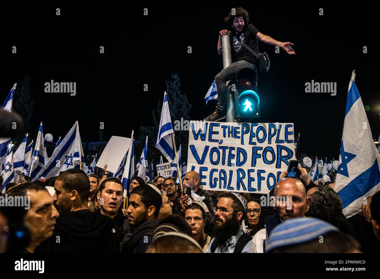 Israel. 27. April 2023. Ein junger Mann sitzt an einer Ampel über einer Menge reformfördernder Demonstranten. Mehr als 200.000 Demonstranten zur Unterstützung der israelischen Regierungen und die umstrittene Gesetzesänderung vor der Knesset. Jerusalem, Israel. April 27. 2023. (Matan Golan/Sipa USA). Kredit: SIPA USA/Alamy Live News Stockfoto