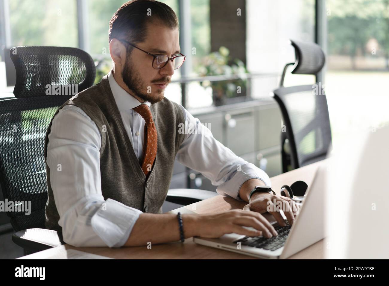 Geschäftsmann aus dem modernen Büro, der am Computer arbeitet. Porträt eines erfolgreichen IT-Software-Ingenieurs mittleren Alters, der an einem Laptop an seinem Schreibtisch arbeitet Stockfoto