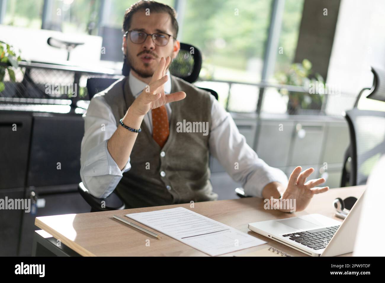 Ein Mann mittleren Alters an einem Schreibtisch, der sich mit einem Kollegen im Büro unterhält und lächelt. Stockfoto