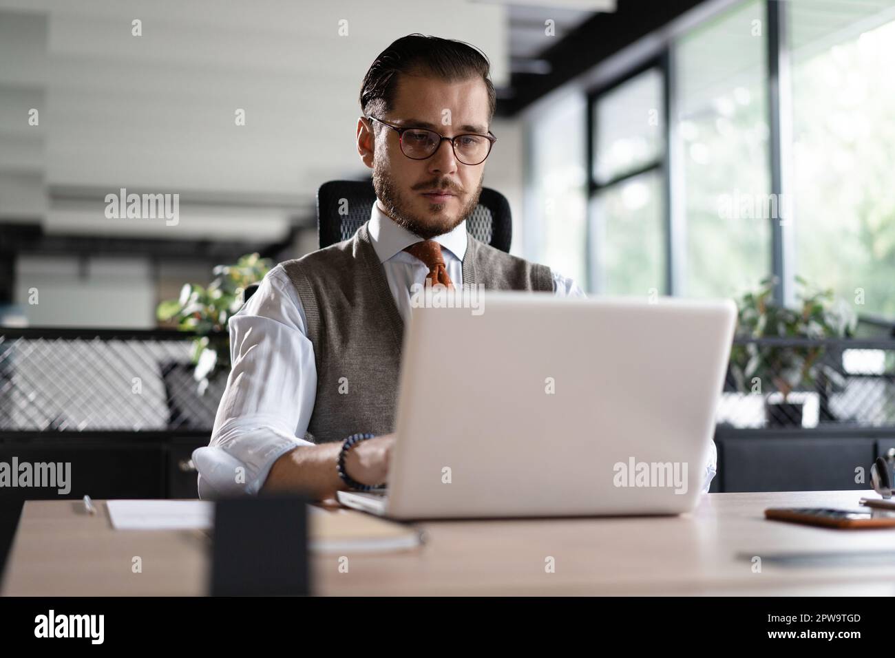 Geschäftsmann aus dem modernen Büro, der am Computer arbeitet. Porträt eines erfolgreichen IT-Software-Ingenieurs mittleren Alters, der an einem Laptop an seinem Schreibtisch arbeitet Stockfoto