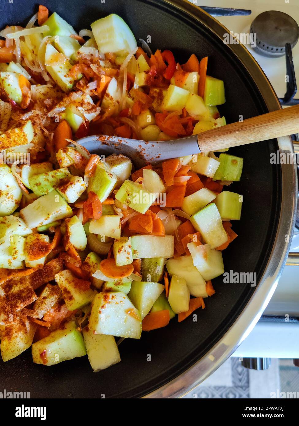 Prozess des Kochens Saute zu Hause. Geschmortes Gemüse und Silikonspatel mit Holzgriff in der Pfanne. Gemischte Zutaten Lauch, Karotte, Zucchini, b Stockfoto