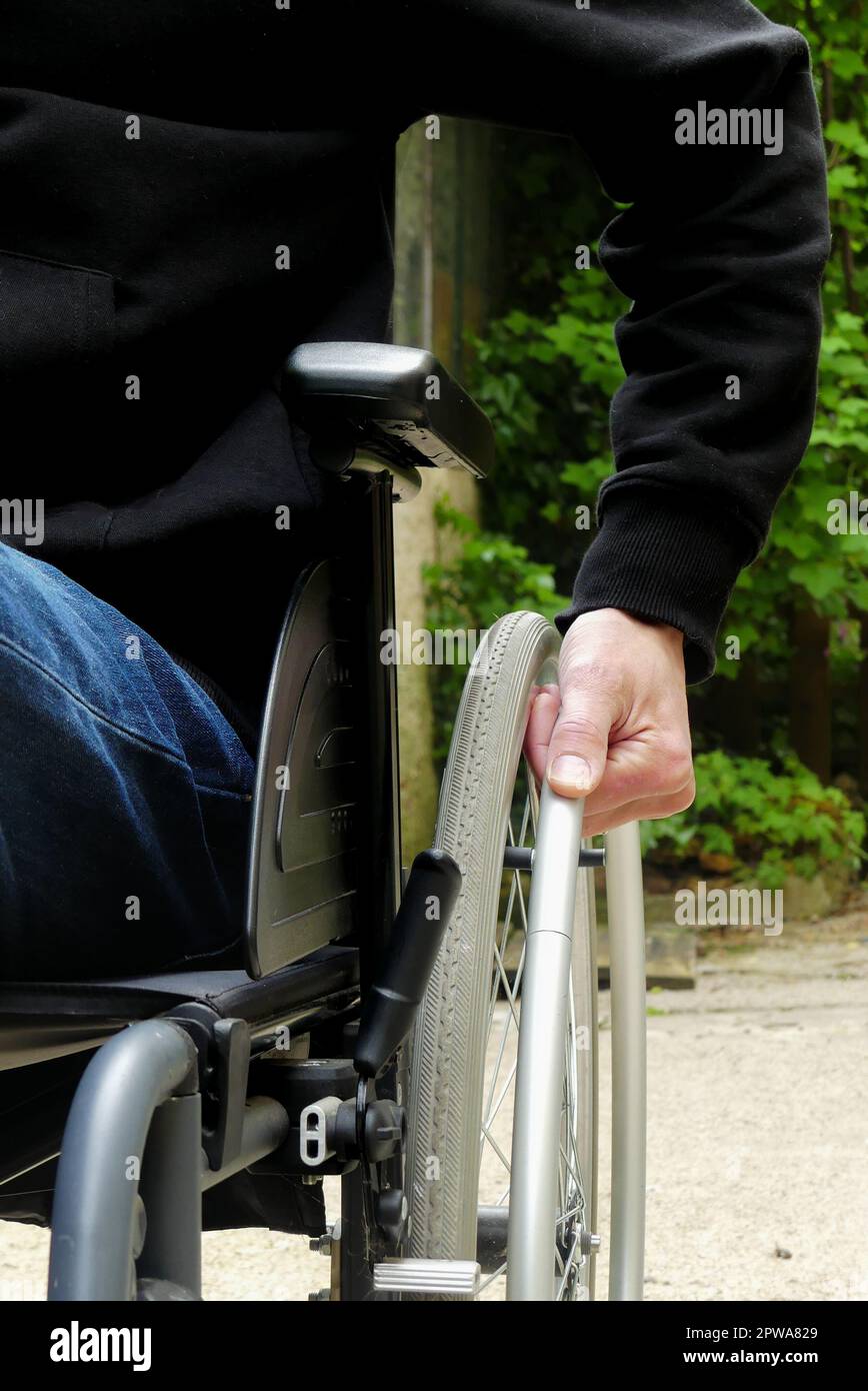 Eine behinderte Person im Rollstuhl. Ein Mann mit eingeschränkter Mobilität in einer Gasse mit Vegetation. Stockfoto