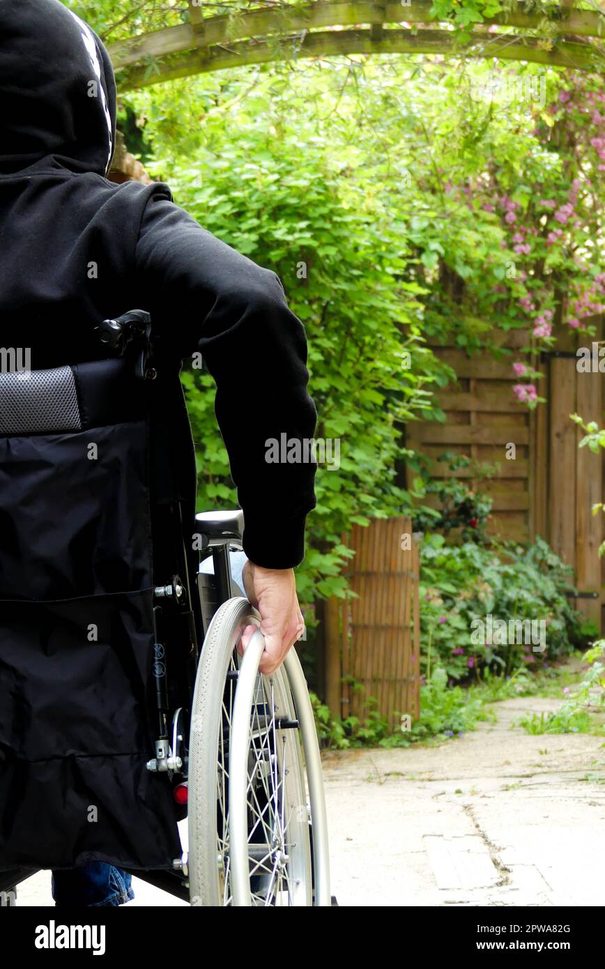 Eine behinderte Person im Rollstuhl. Ein Mann mit eingeschränkter Mobilität in einer Gasse mit Vegetation. Stockfoto