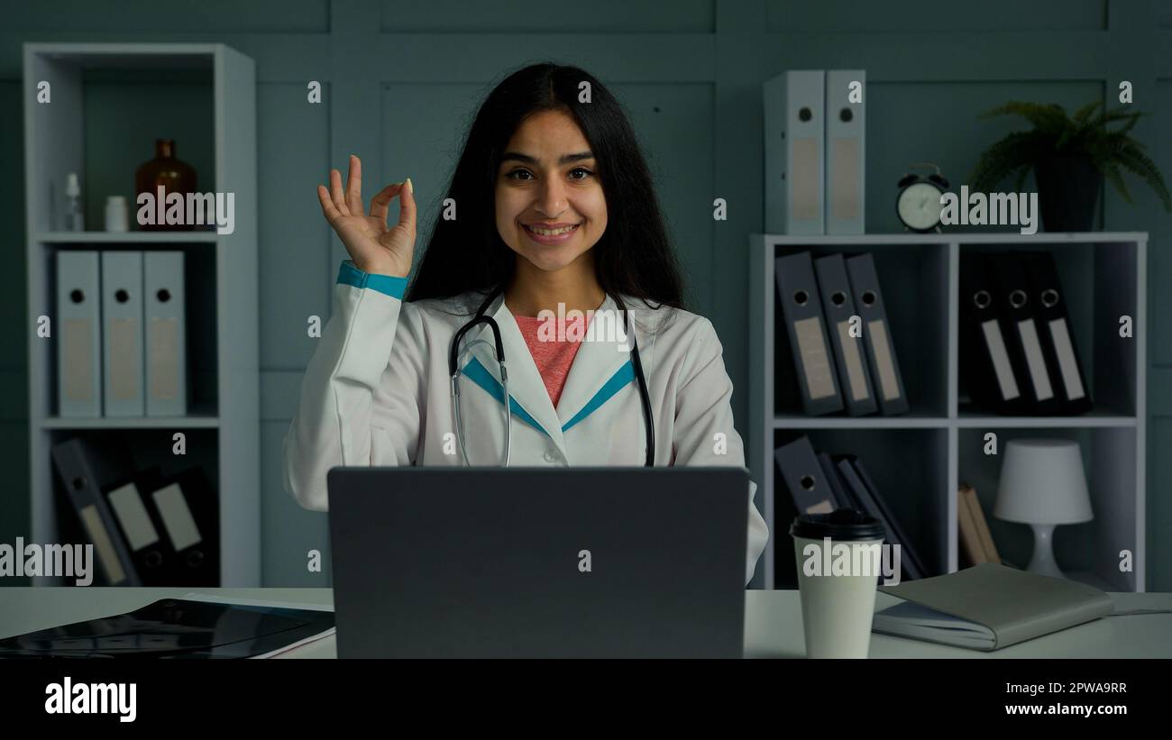 Glückliche positive junge Frau Doktor arabian indianer Ethnisch Therapeutin Arzt schaut auf Kamera lächeln machen okay Handgeste empfehlen gut Stockfoto