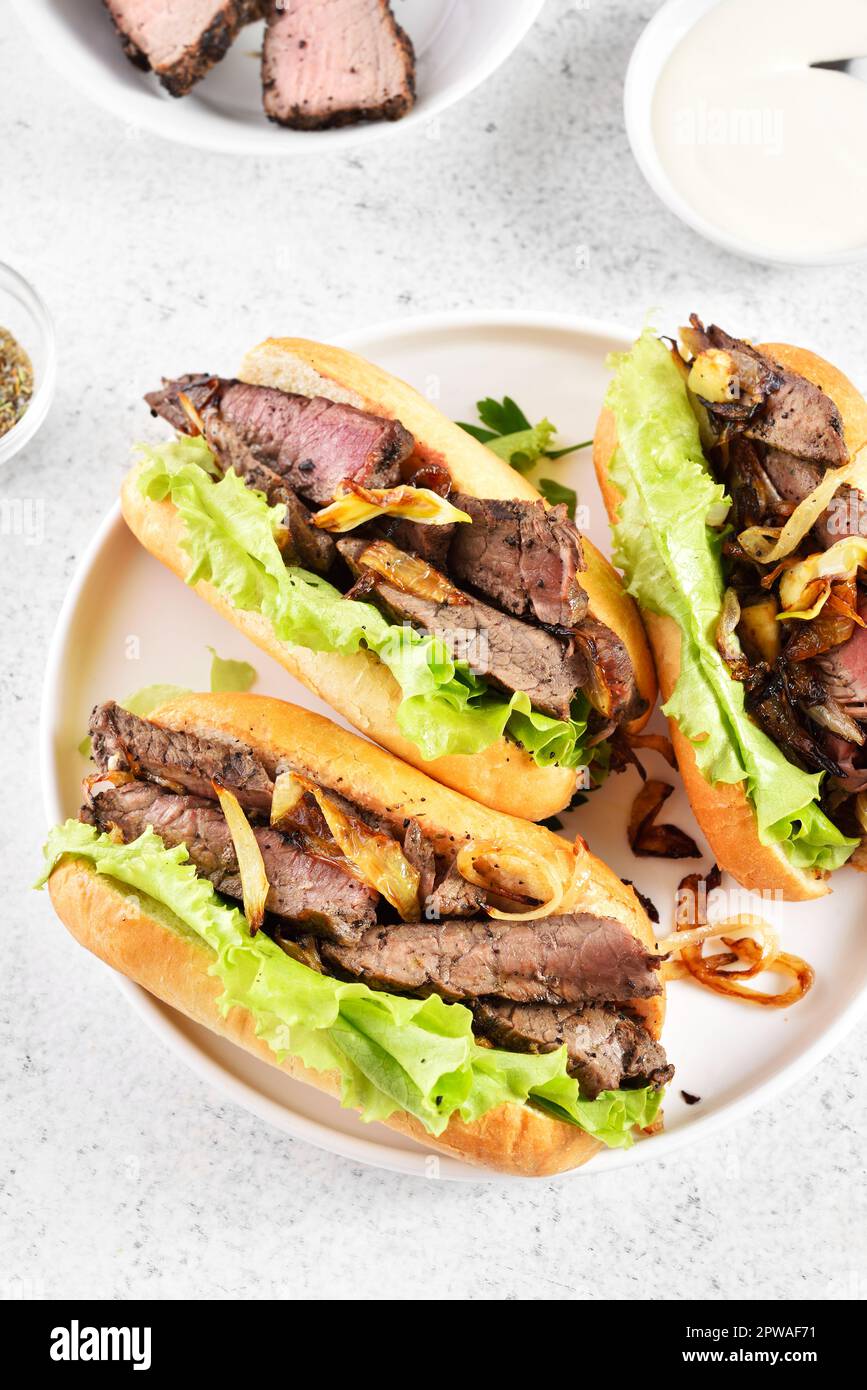 Sandwiches mit Rindfleisch und karamellisierten Zwiebeln auf dem Teller auf hellem Steinhintergrund. Nahaufnahme Stockfoto