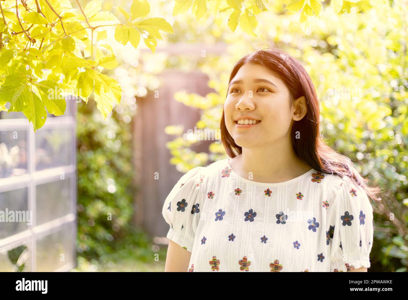 Glückliche Frau junger Teenager, der im Garten lächelt, mit grünem Baum, frischer Umgebung, Luftökologie im Garten Stockfoto